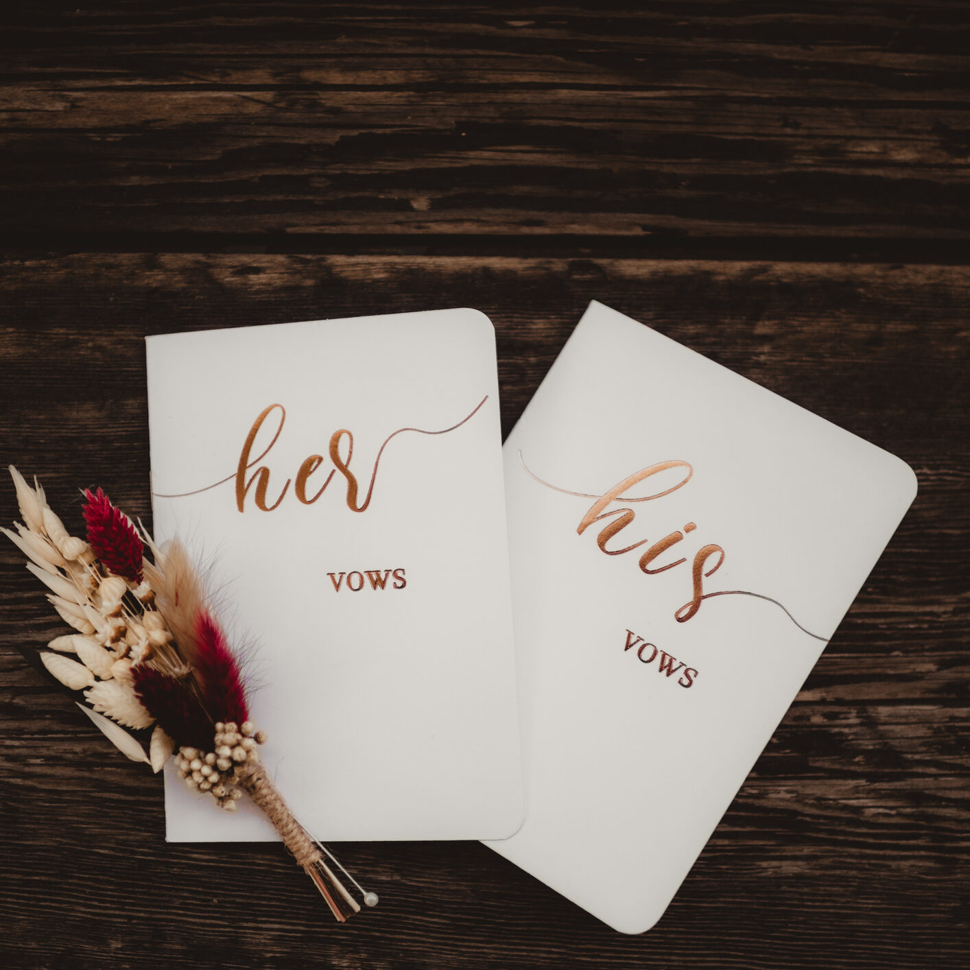 His and Hers wedding vows books with dried flowers on wood floor